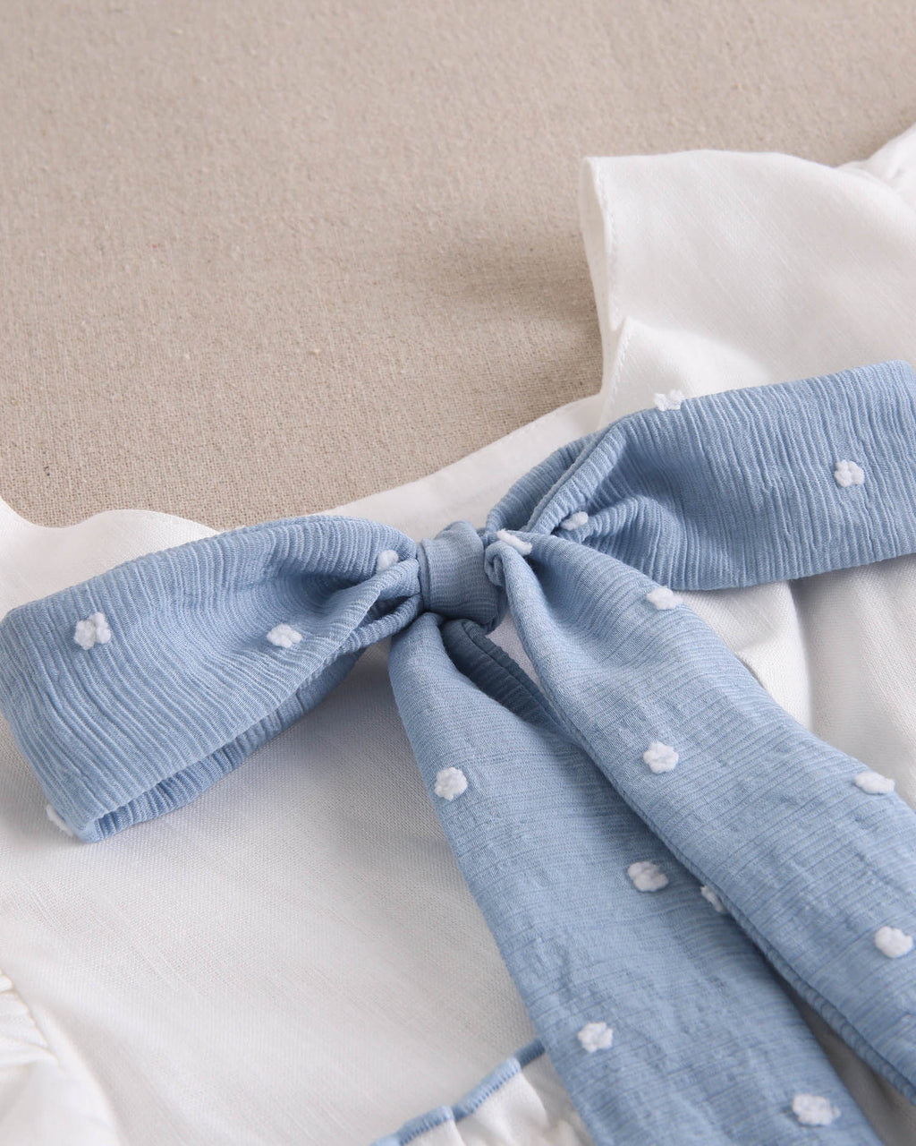 Vestido niña blanco con bordes en azul y lazo en espalda de plumeti azul