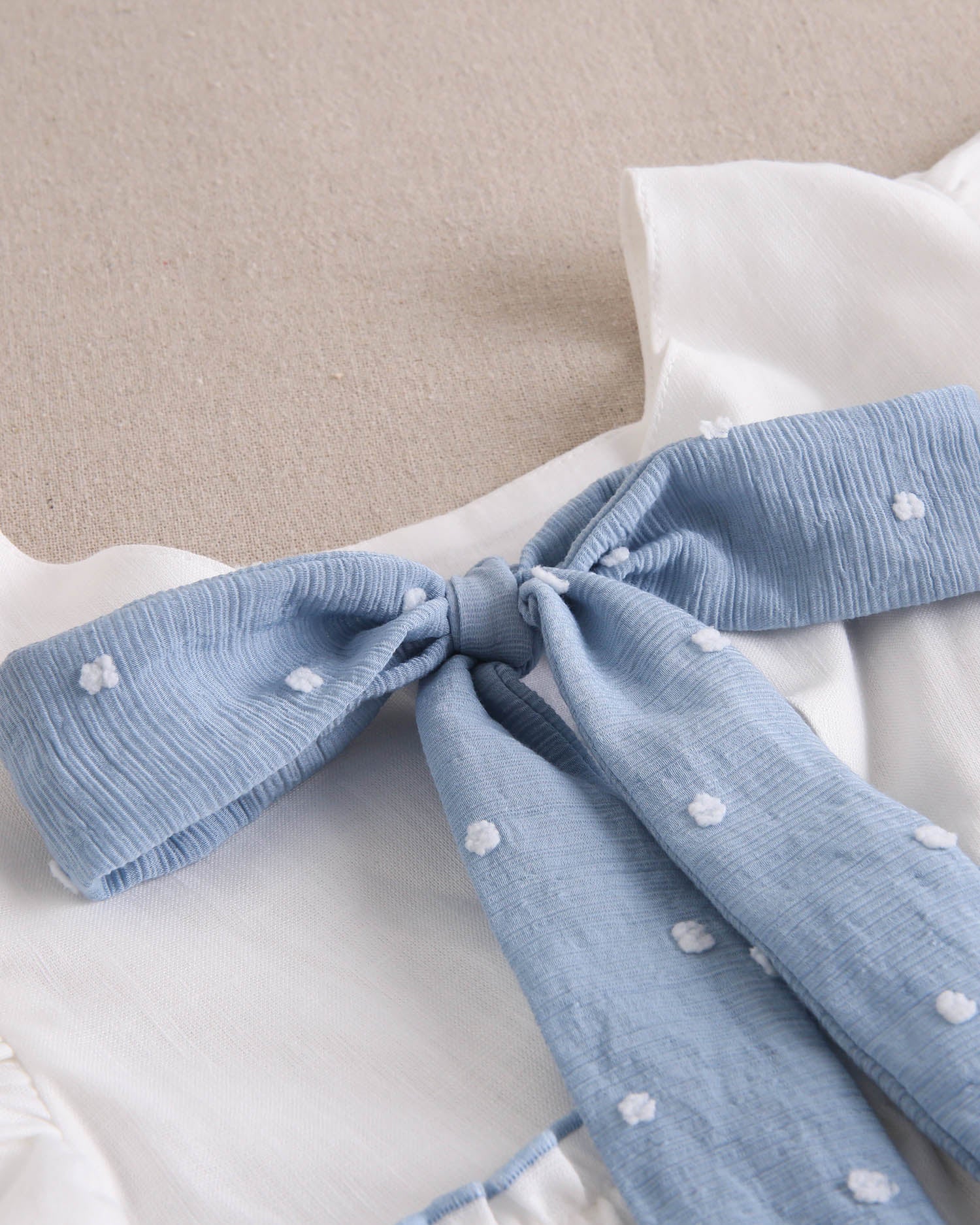 Vestido niña blanco con bordes en azul y lazo en espalda de plumeti azul