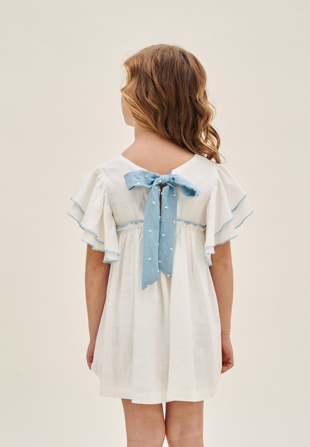 Vestido niña blanco con bordes en azul y lazo en espalda de plumeti azul