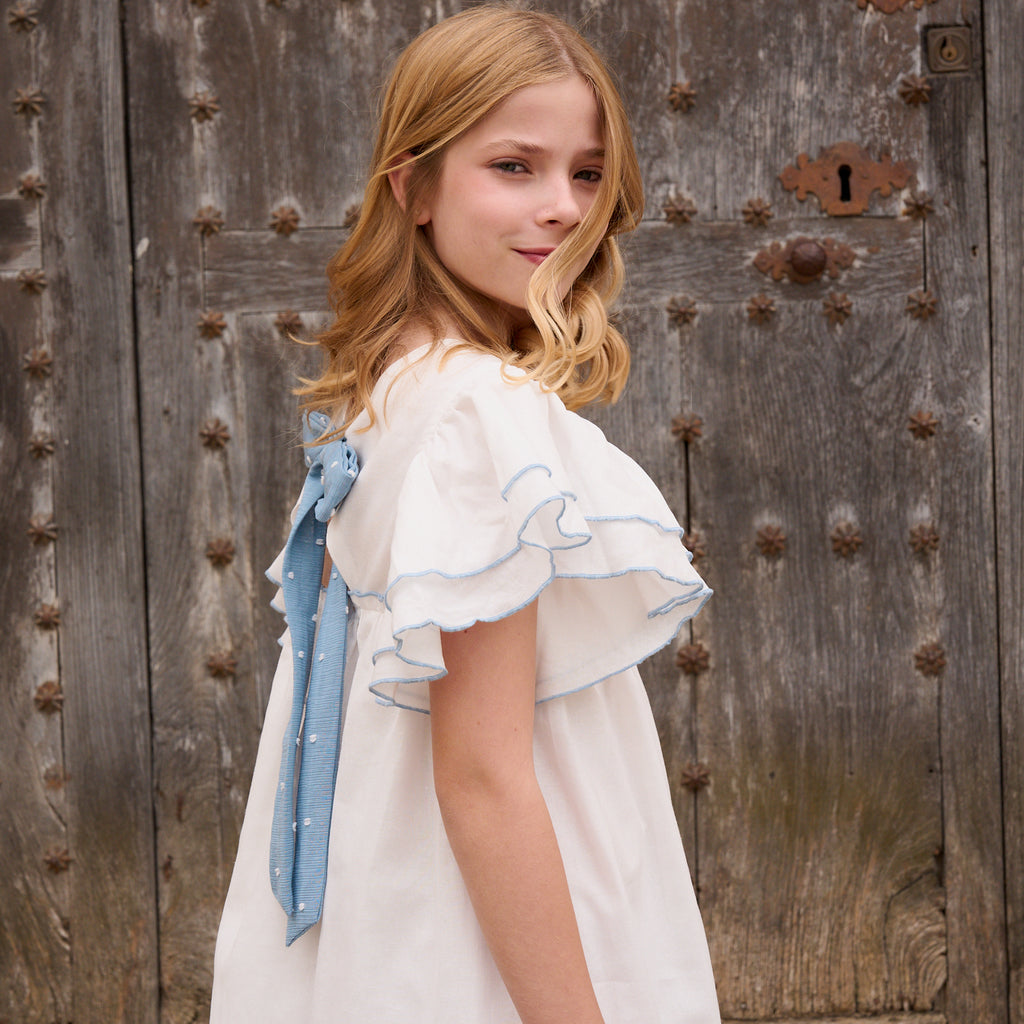 Vestido niña blanco con bordes en azul y lazo en espalda de plumeti azul