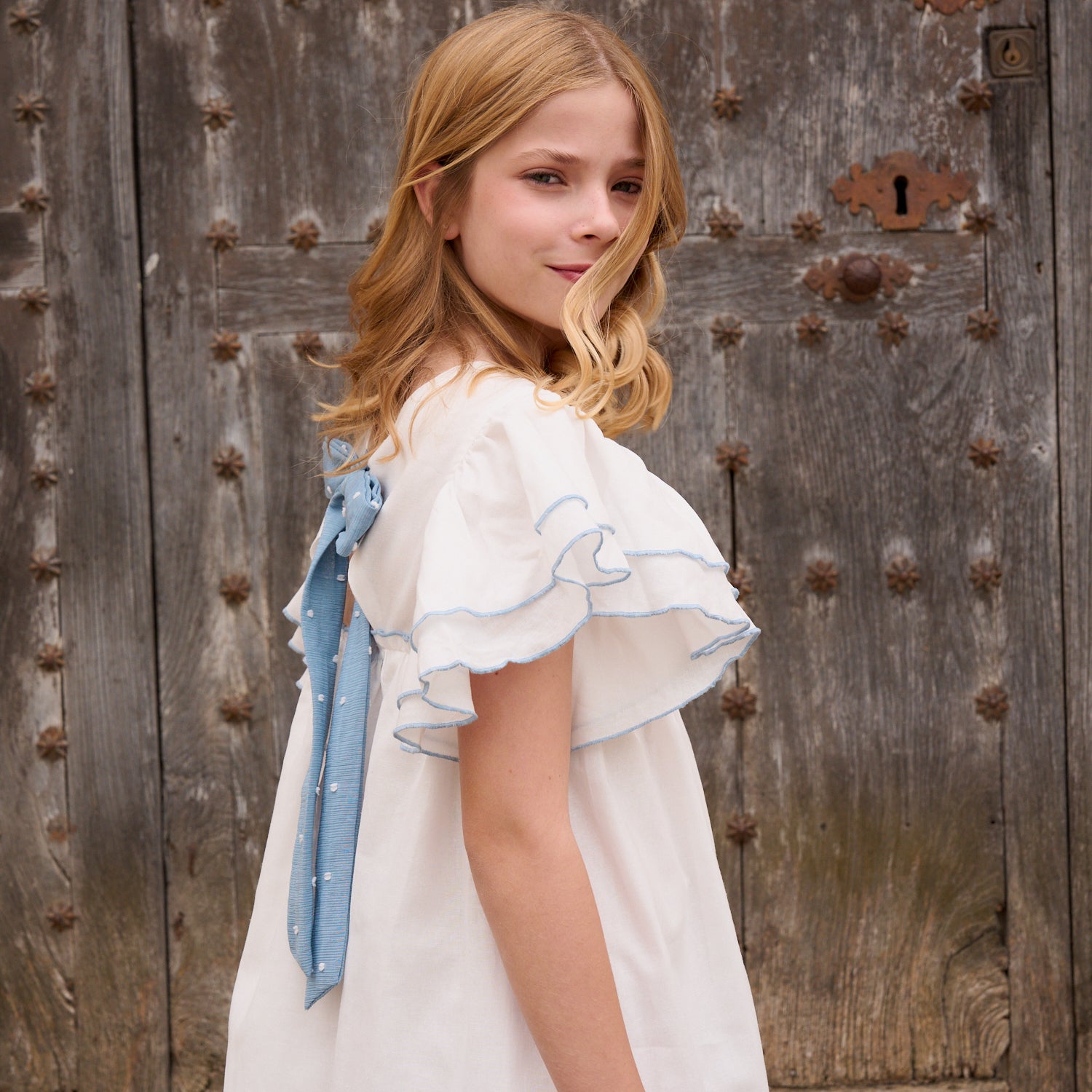 Vestido niña blanco con bordes en azul y lazo en espalda de plumeti azul