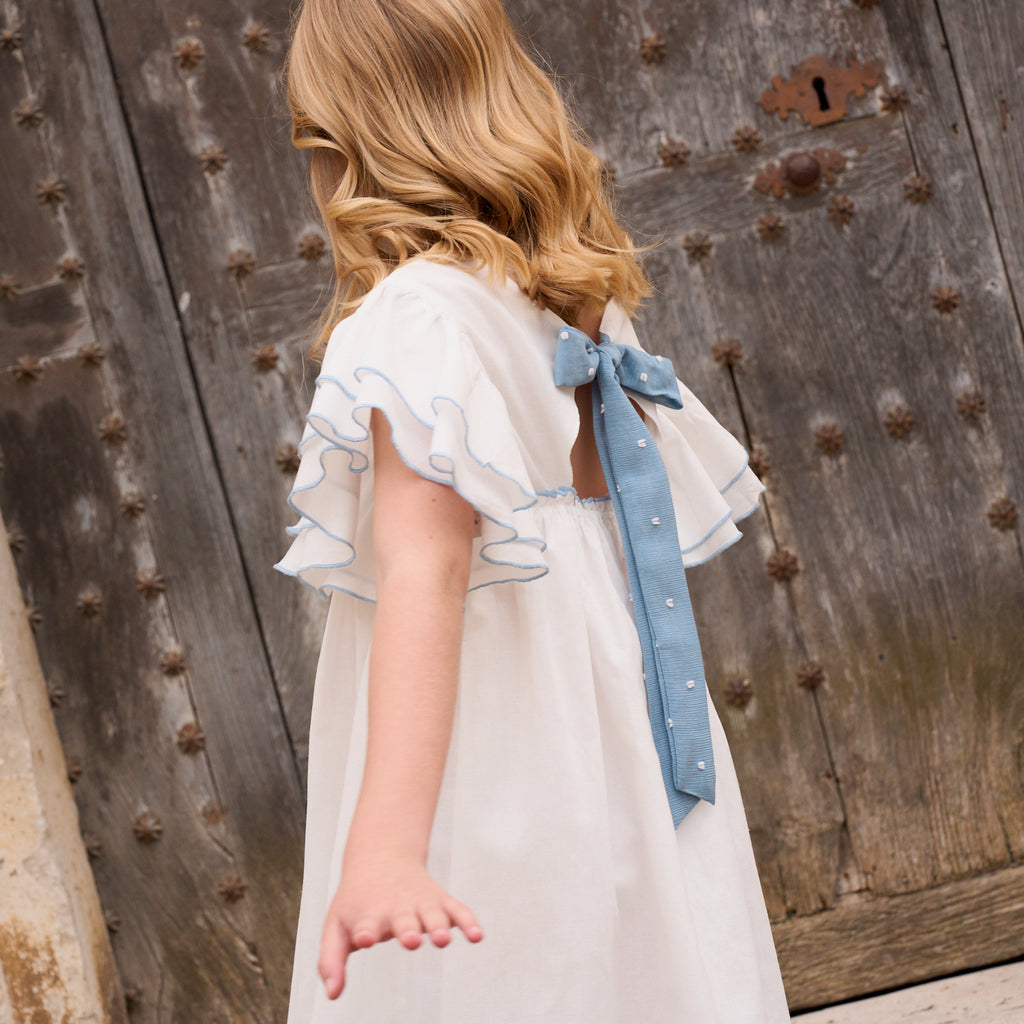 Vestido niña blanco con bordes en azul y lazo en espalda de plumeti azul
