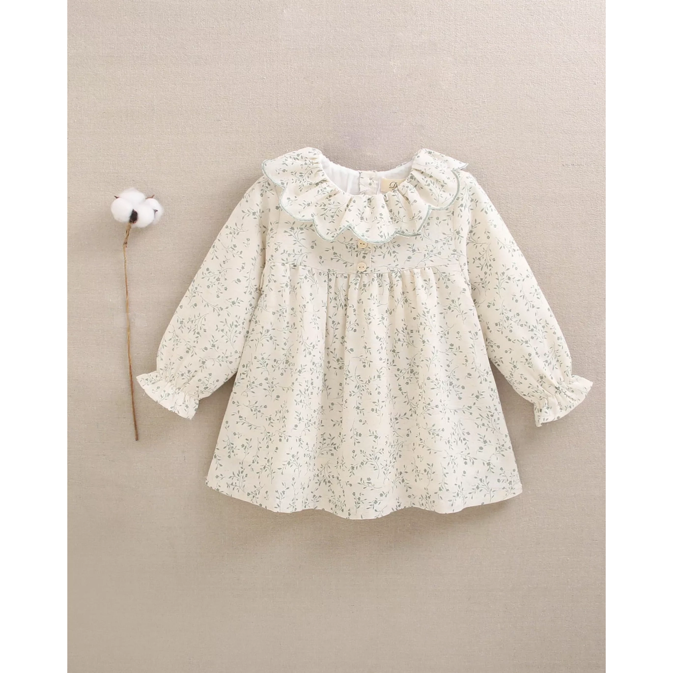 Vestido de bebé color crudo con estampado floral verde y volante en el cuello
