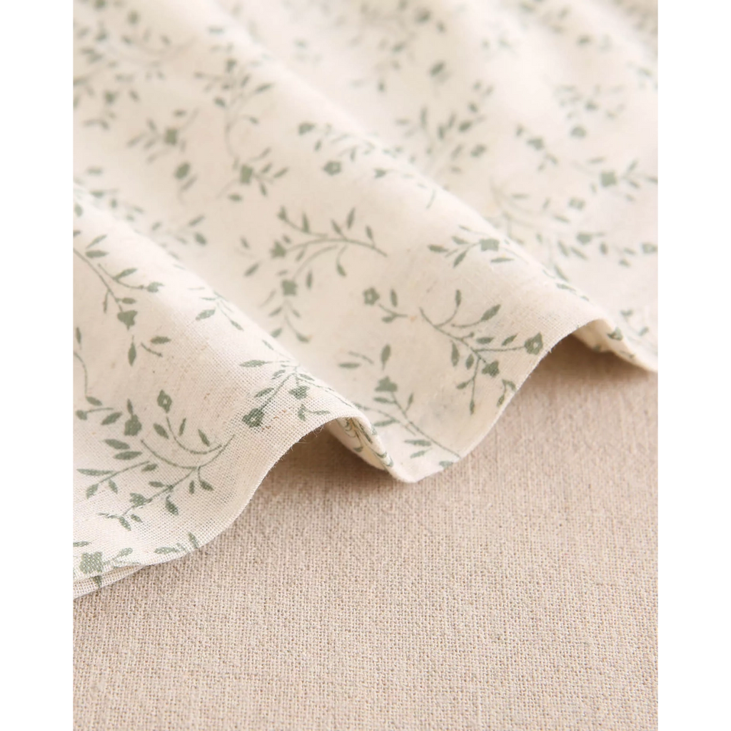 Vestido de bebé color crudo con estampado floral verde y volante en el cuello